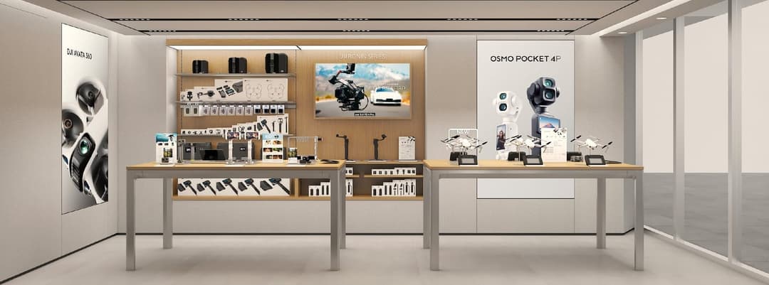 The image shows a modern store display for the DJI Ronin series, featuring a sleek black and white color scheme. The display is set against a light beige or cream-colored wall, with a large window on the right side. The display includes a black table with a white top, displaying a variety of DJI products such as camera