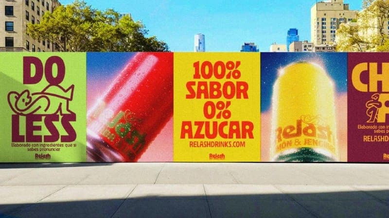 The image shows a vibrant advertisement for Relash drinks, featuring a large yellow billboard with the text "100% SABOR 0% AZUCAR" and the Relash logo. The billboard also includes a picture of a red Relash drink can with a green label. To the left of the billboard, a green billboard displays the text "DO LESS" and a ca