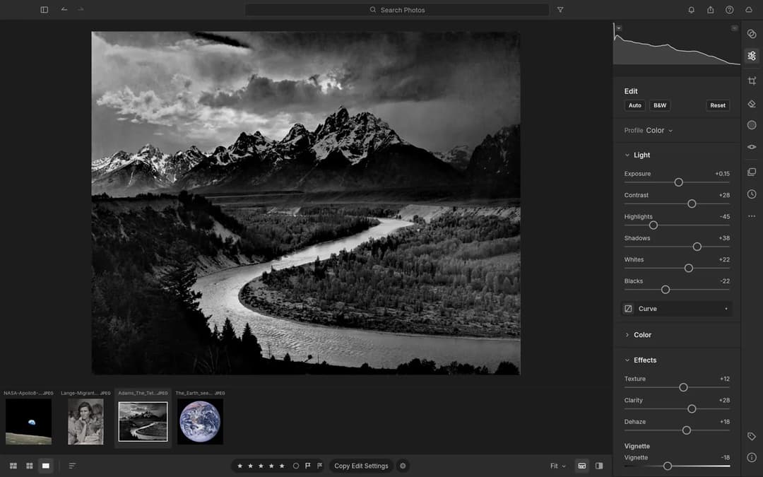 The image is a black and white photograph of a winding river flowing through a mountainous landscape. The photograph is taken from a high vantage point, showcasing the grandeur of the mountains and the river's meandering path. The sky is filled with clouds, adding depth to the scene. The photograph is presented in a ph