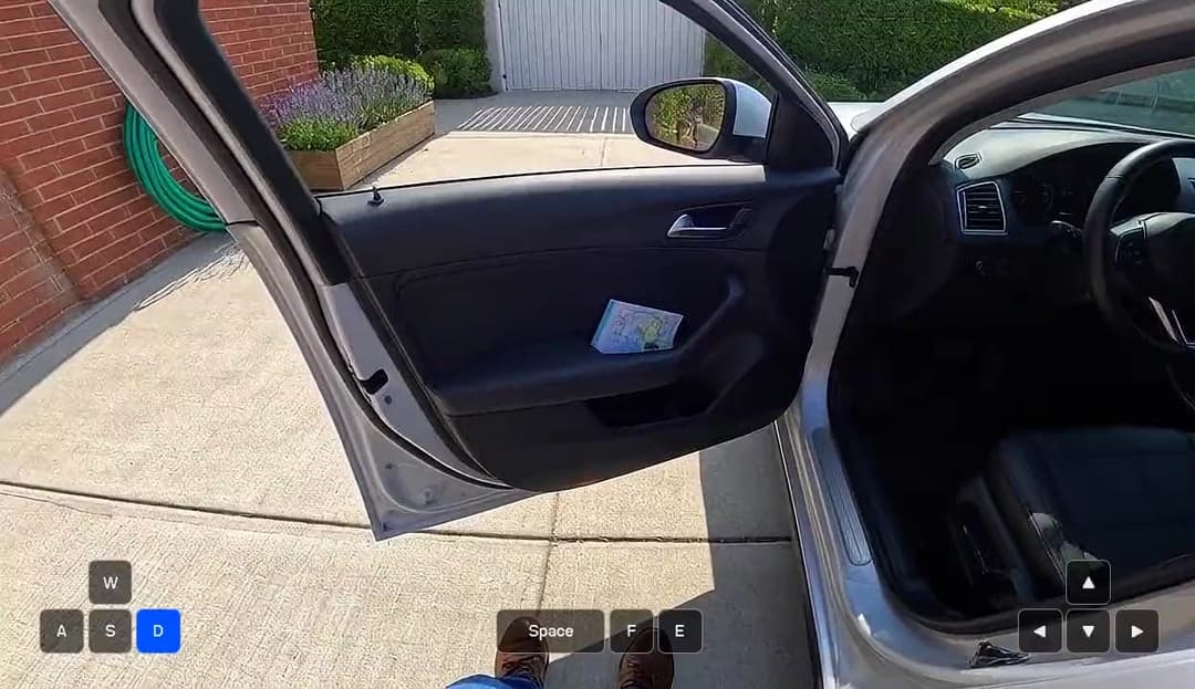 The image shows a silver car parked on a driveway in front of a brick wall. The car's door is open, revealing a small piece of paper or a map inside. A green hose is visible on the left side of the image. The car's interior is dark, and the driver's side door is open. The image is taken from a low angle, giving the imp