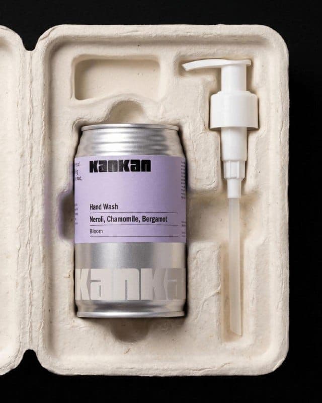 The image shows a silver can of Kankan Hand Wash nestled in a white cardboard box. The can is labeled with the brand name "Kankan" and the product name "Hand Wash" in black text. The box has a cut-out design for dispensing the hand wash, and a white pump dispenser is attached to the side of the can. The can also featur