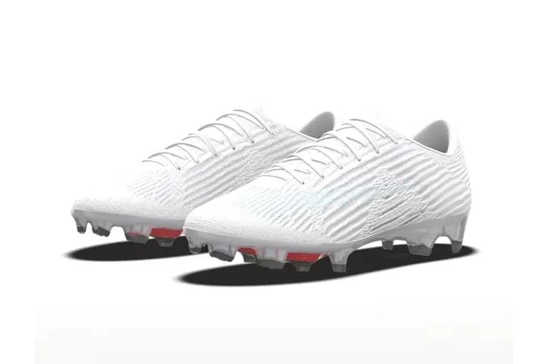 The image presents a pair of white soccer cleats, each with a unique red sole, positioned on a white background. The cleats are oriented towards the right side of the image, with the toes pointing towards the left. The laces of the cleats are neatly tied, and the soles feature a textured pattern. The cleats appear to b