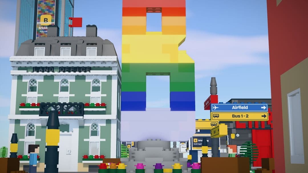 The image depicts a vibrant cityscape constructed from Lego bricks. A large, rainbow-colored Lego structure dominates the center of the image, with a smaller, multi-colored Lego building to its left. The cityscape features a variety of buildings, including a green building with a sign that reads "Land Office" and a red