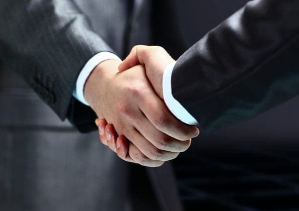 Close-up of two people in dark business suits shaking hands, with white shirt cuffs visible.