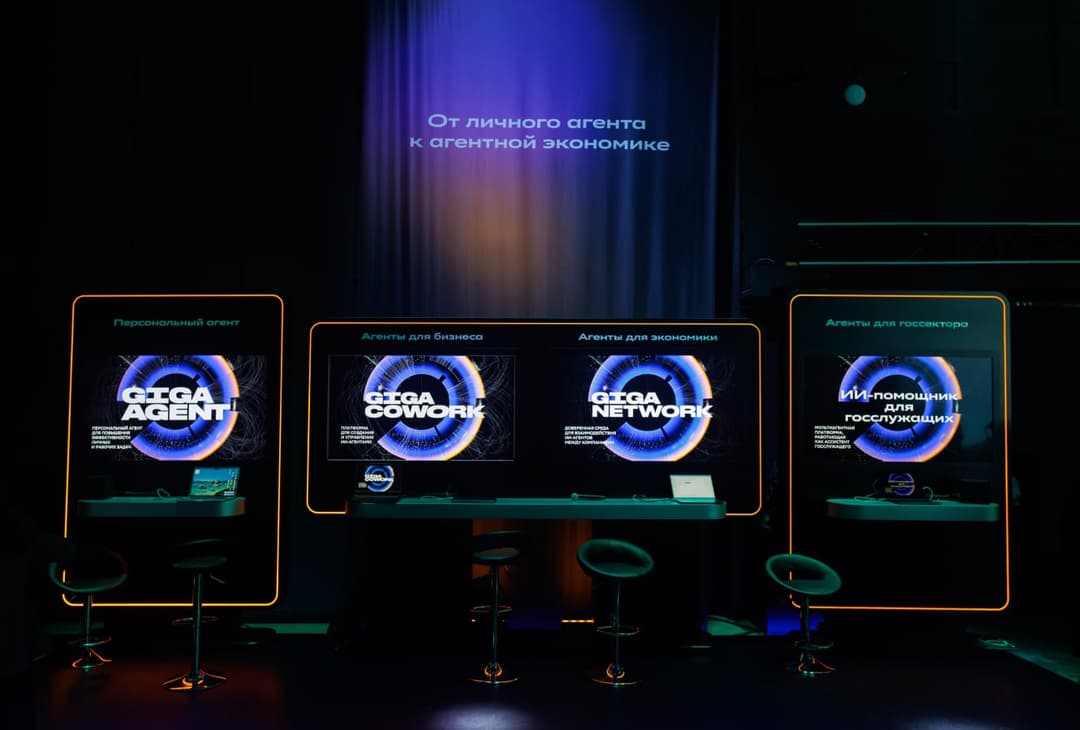 The image shows a stage with three large screens displaying the text "������������������ ������������������ ����������������������������������������" in a dark blue/purple color scheme. The screens are arranged in a row, with the middle screen slightly larger than the two on either side