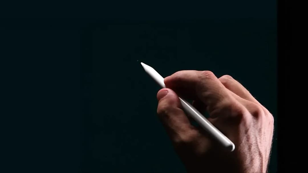 The image shows a hand holding a white pen, poised to write on a dark, possibly black, surface. The hand is positioned in the center of the frame, with the pen held in a way that suggests it is ready to make a mark. The pen is held in a way that suggests it is ready to write. The hand and pen are the only objects in th