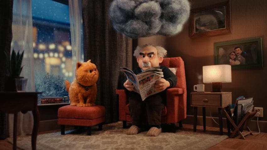 In a cozy living room, a man with a mustache and gray hair is seated in a red armchair, engrossed in reading a newspaper titled "De Gelder". A ginger cat sits on a small red ottoman beside him. The room is bathed in soft light, with a large gray cloud hanging from the ceiling. The room is decorated with framed pictures