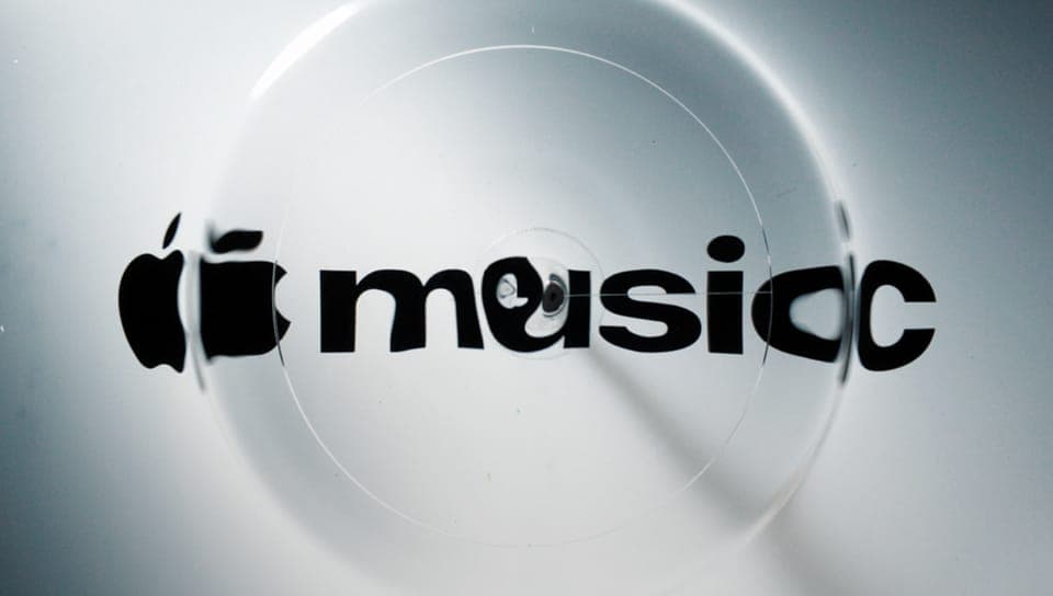 The image shows a close-up view of a white surface with a circular pattern, possibly a CD or vinyl record, that has a slight distortion or ripple effect. The surface features the Apple logo in black, with the word "music" written in a stylized, black font. The logo and the word "music" are slightly distorted, giving th