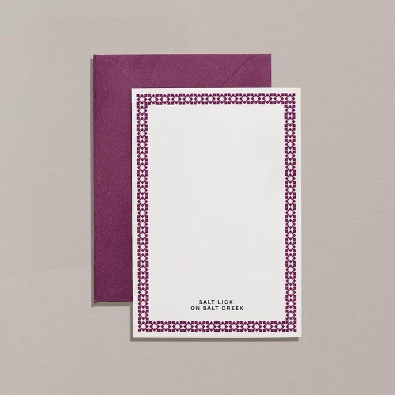The image shows a rectangular white card with a maroon border featuring a repeating geometric pattern. The card is placed on a light beige background. The text "Salt Lick on Salt Creek" is printed in black at the bottom of the card. The card is slightly tilted to the right.
