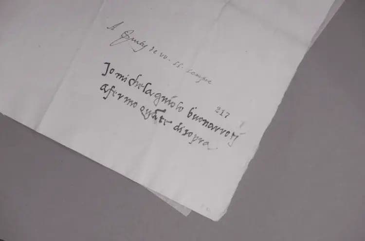 The image shows a piece of white paper with black handwritten text. The text appears to be a message or note, written in a cursive style. The text is written in a language that is not English, and it is unclear if it is a formal message or a casual note. The paper is slightly crumpled, and the writing is not perfectly