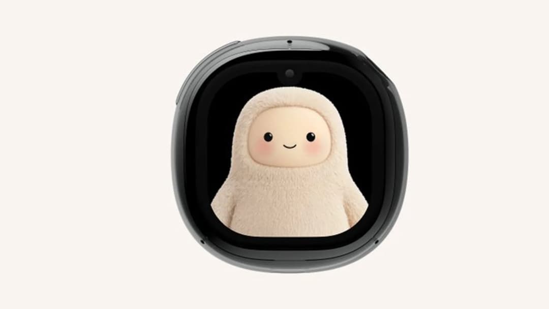 The image shows a black smartphone with a rounded edge, featuring a small, round camera lens at the top. The phone's screen is black and displays a cartoon character with a white, furry body and a friendly, smiling face. The character has large, round eyes and rosy cheeks. The phone is positioned against a light beige
